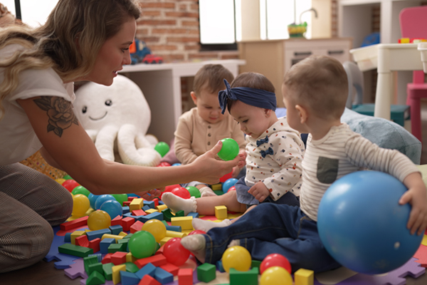 teacher and three young children sitting on the floor playing with a heap of colorful balls and blocks