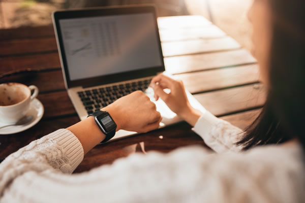 woman sitting in front of a laptop computer and looking at the watch on her wrist